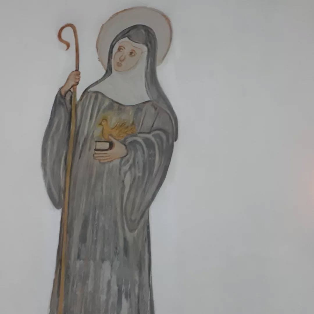 Santa Escolástica pintada na parede da igreja, com o báculo e a pomba nas mãos.