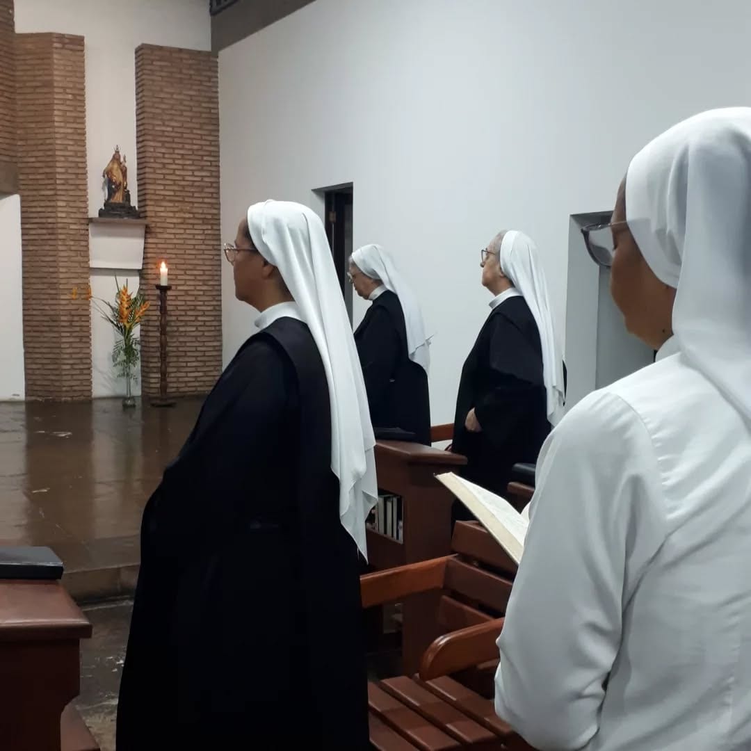 Monjas de pé no coro, com os livros abertos, durante a oração.
