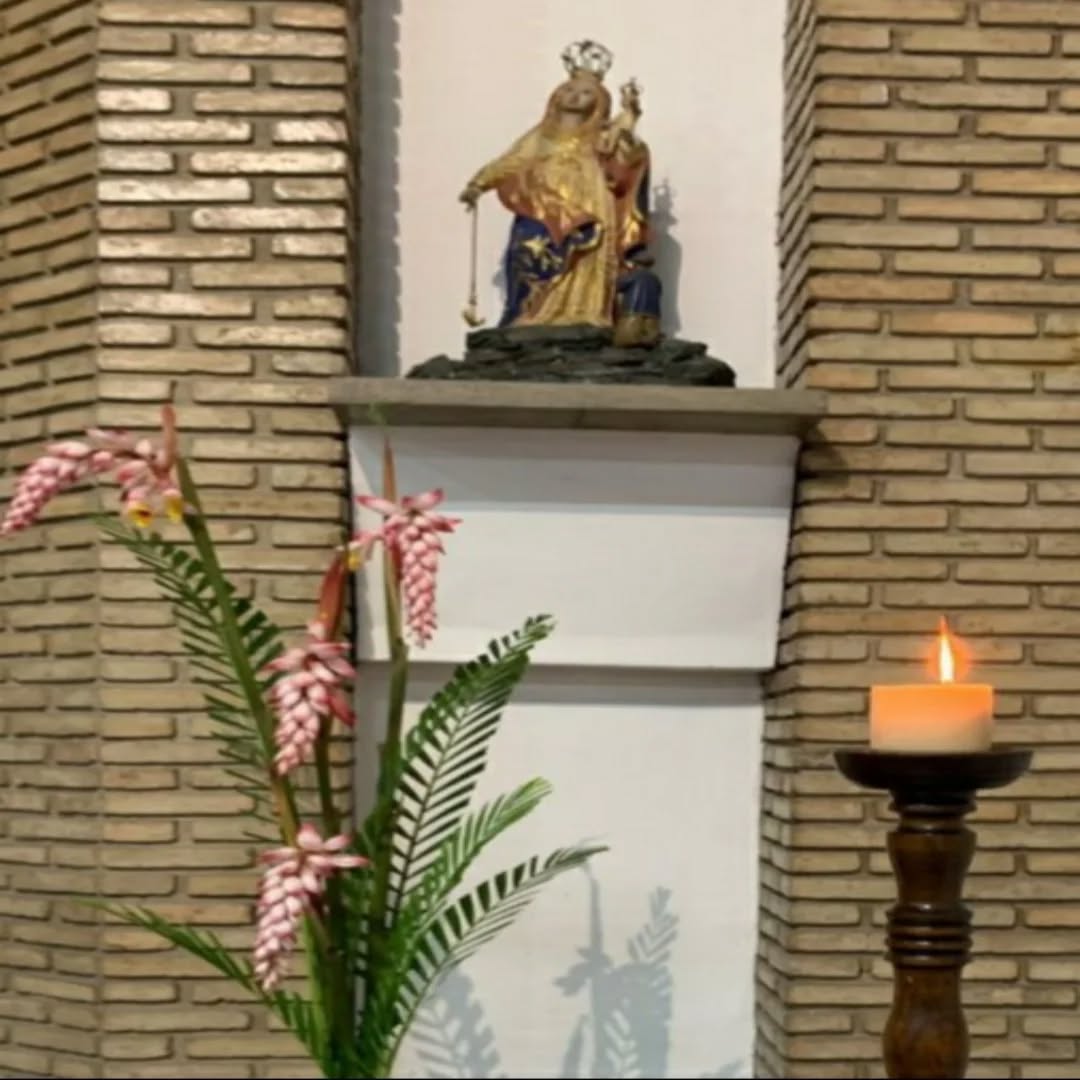 Imagem de Nossa Senhora sobre a mísula de tijolo, com flores e uma vela acesa ao lado.