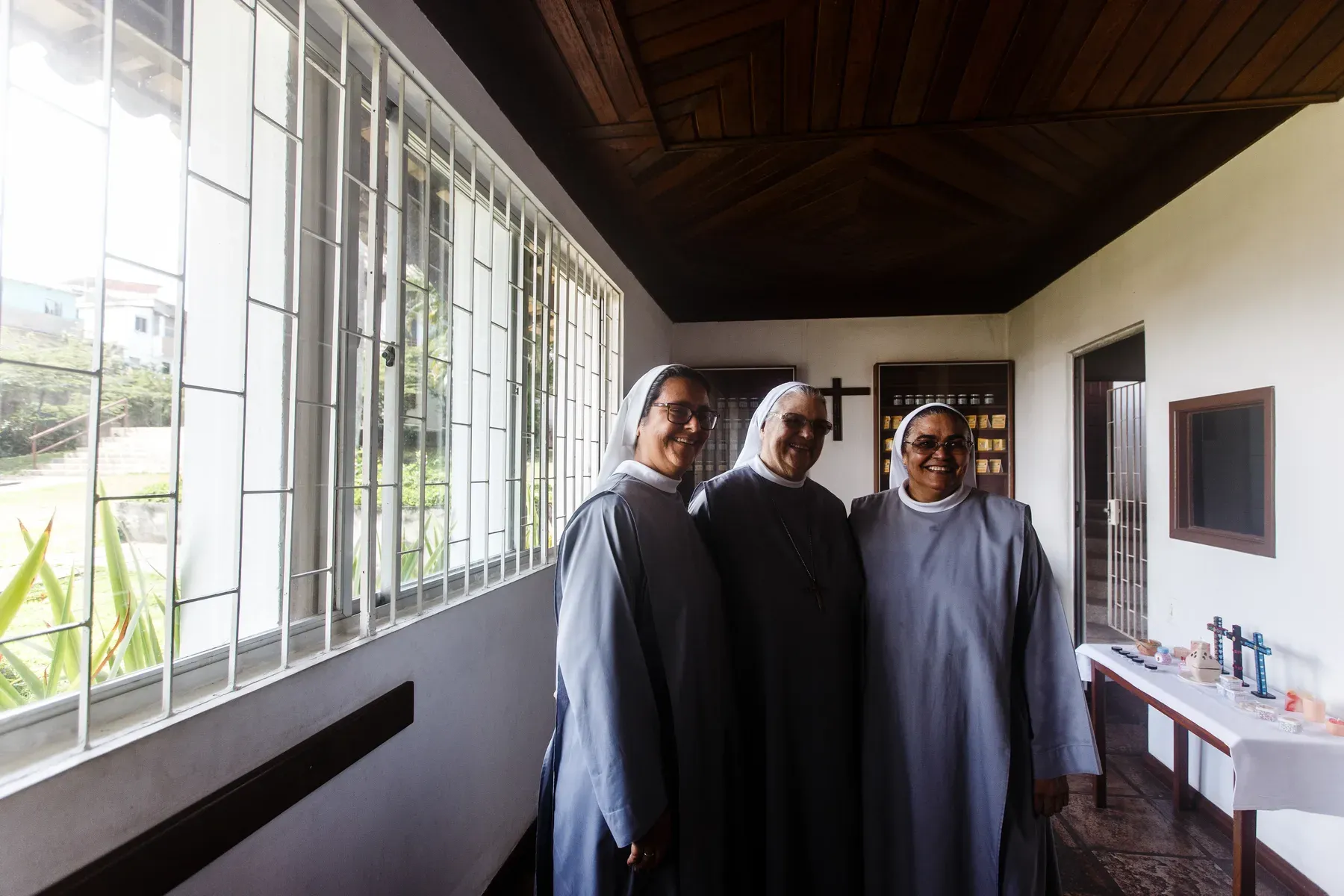 Monjas beneditinas no corredor envidraçado, com o bosque ao fundo