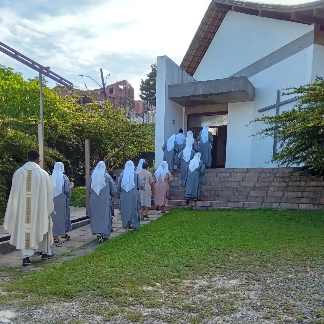 A comunidade atravessa o gramado a caminho da igreja, atrás do celebrante.